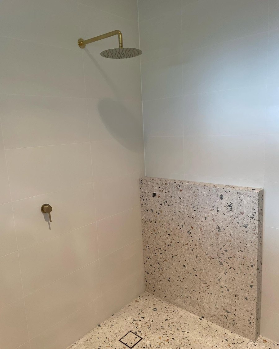 Shower with a brass rain shower head and a terrazzo nib wall